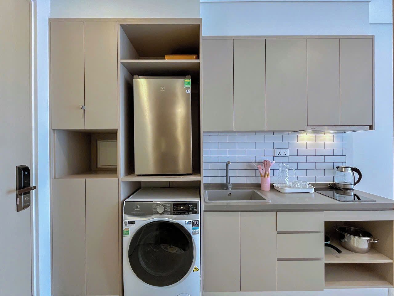 Cocina compacta con lavadora y secadora integradas, refrigerador de acero inoxidable y un lavamanos con hervidor.