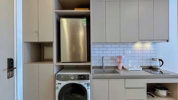 Cocina compacta con lavadora y secadora integradas, refrigerador de acero inoxidable y un lavamanos con hervidor.