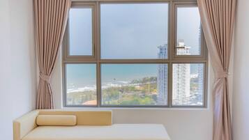 A room with a large window, beige curtains, and a beige sofa.