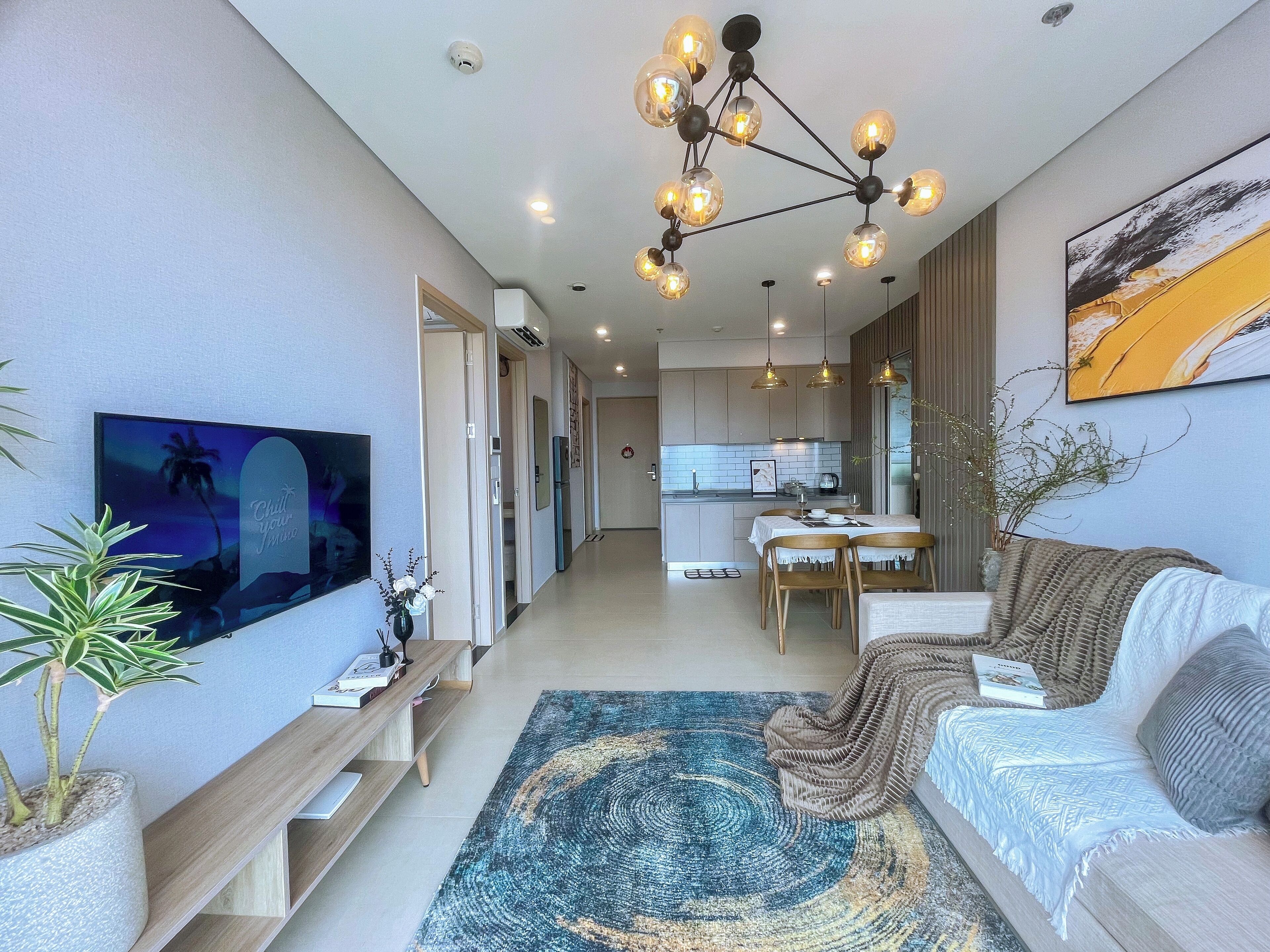 A modern living room with a sofa, TV, and a dining area with a kitchen in the background.