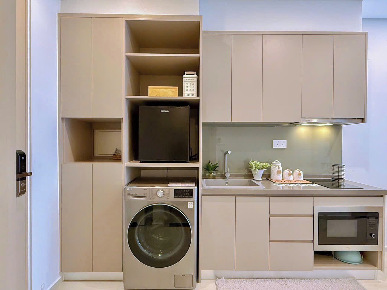 A compact kitchen with a washing machine, microwave, and a small refrigerator.