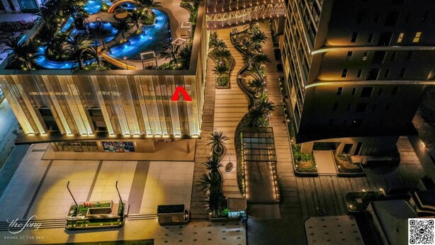 Vista aérea de un hotel con piscina, palmeras y fachada de edificio moderno.