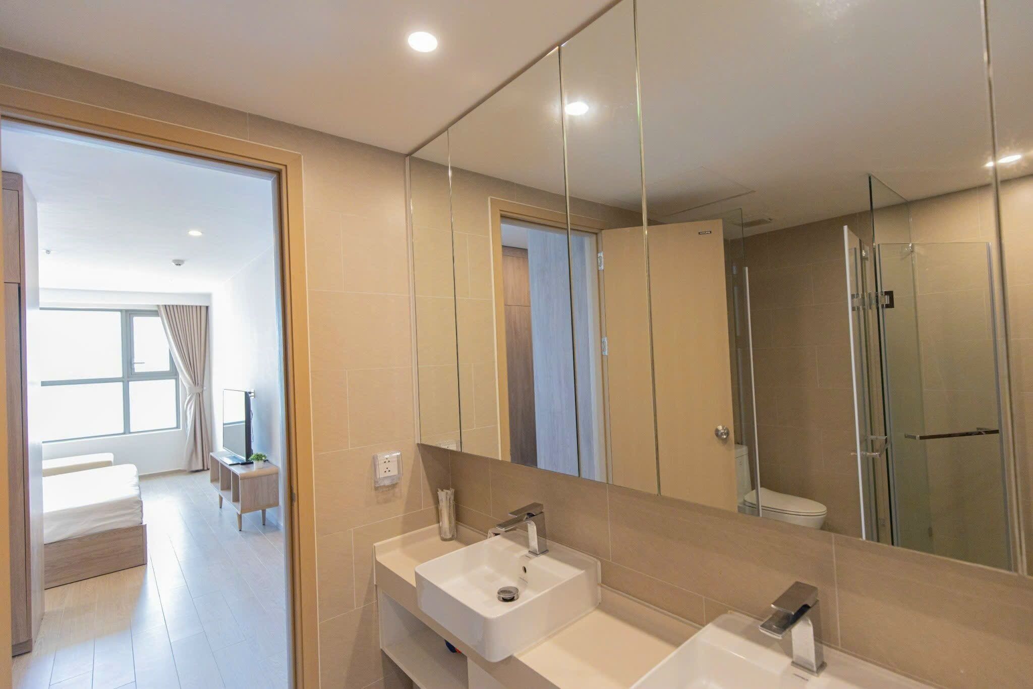 A modern bathroom with a large mirror, two sinks, and a shower.