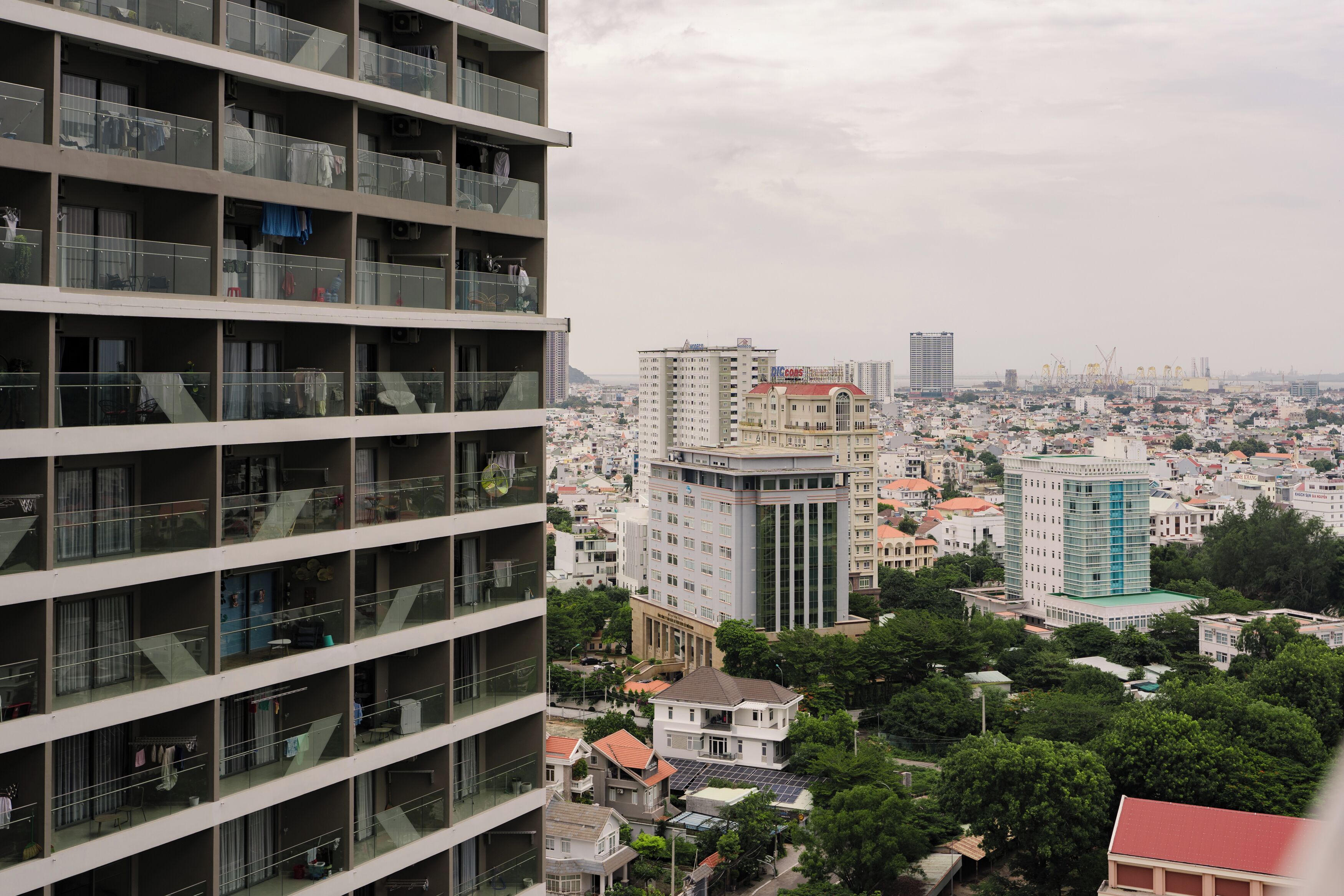 A high-rise building with multiple balconies, a mix of residential and commercial buildings in the background, and a cloudy sky.