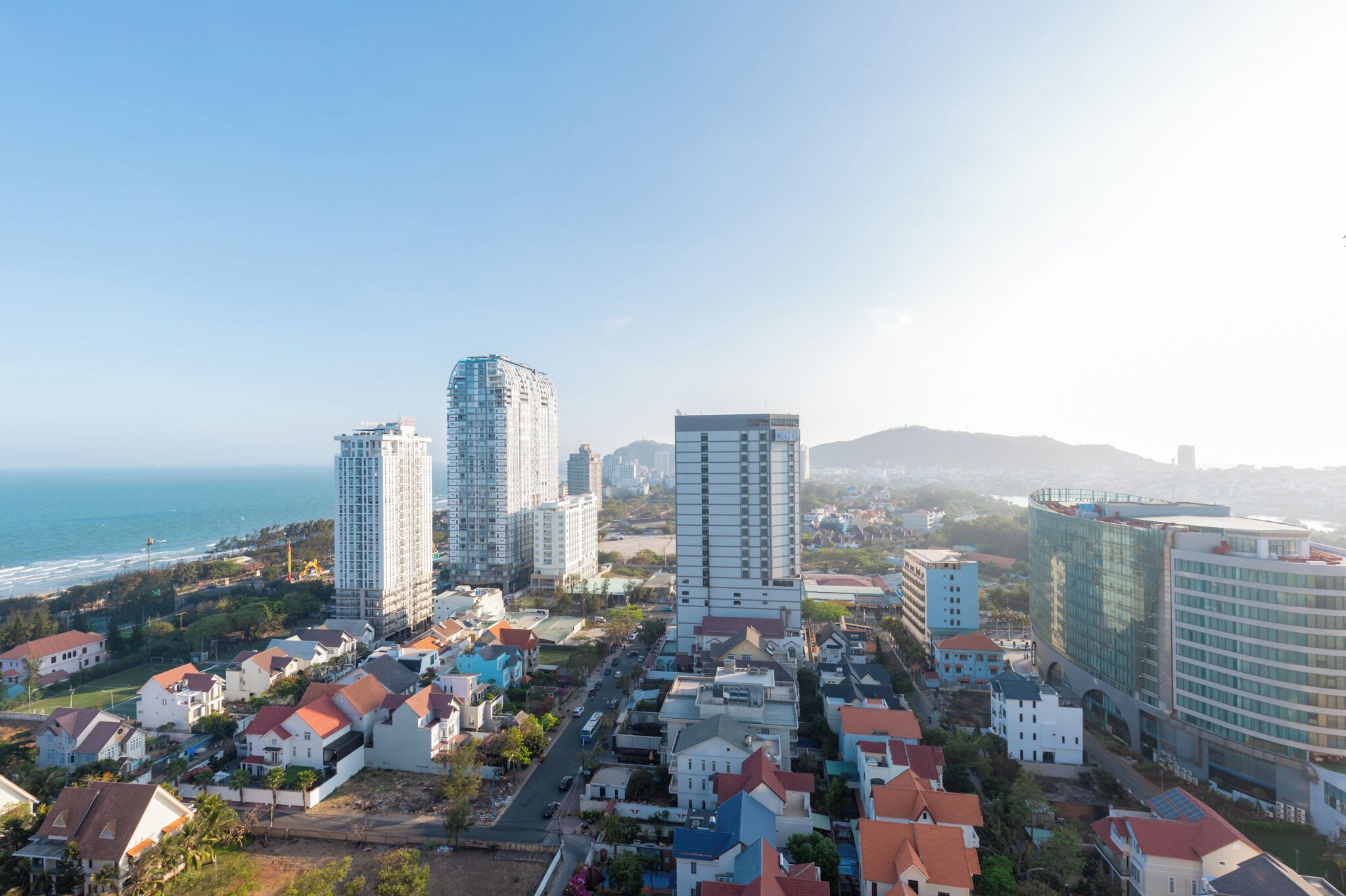 A coastal cityscape with high-rise buildings, a mix of residential and commercial structures, and a view of the ocean.