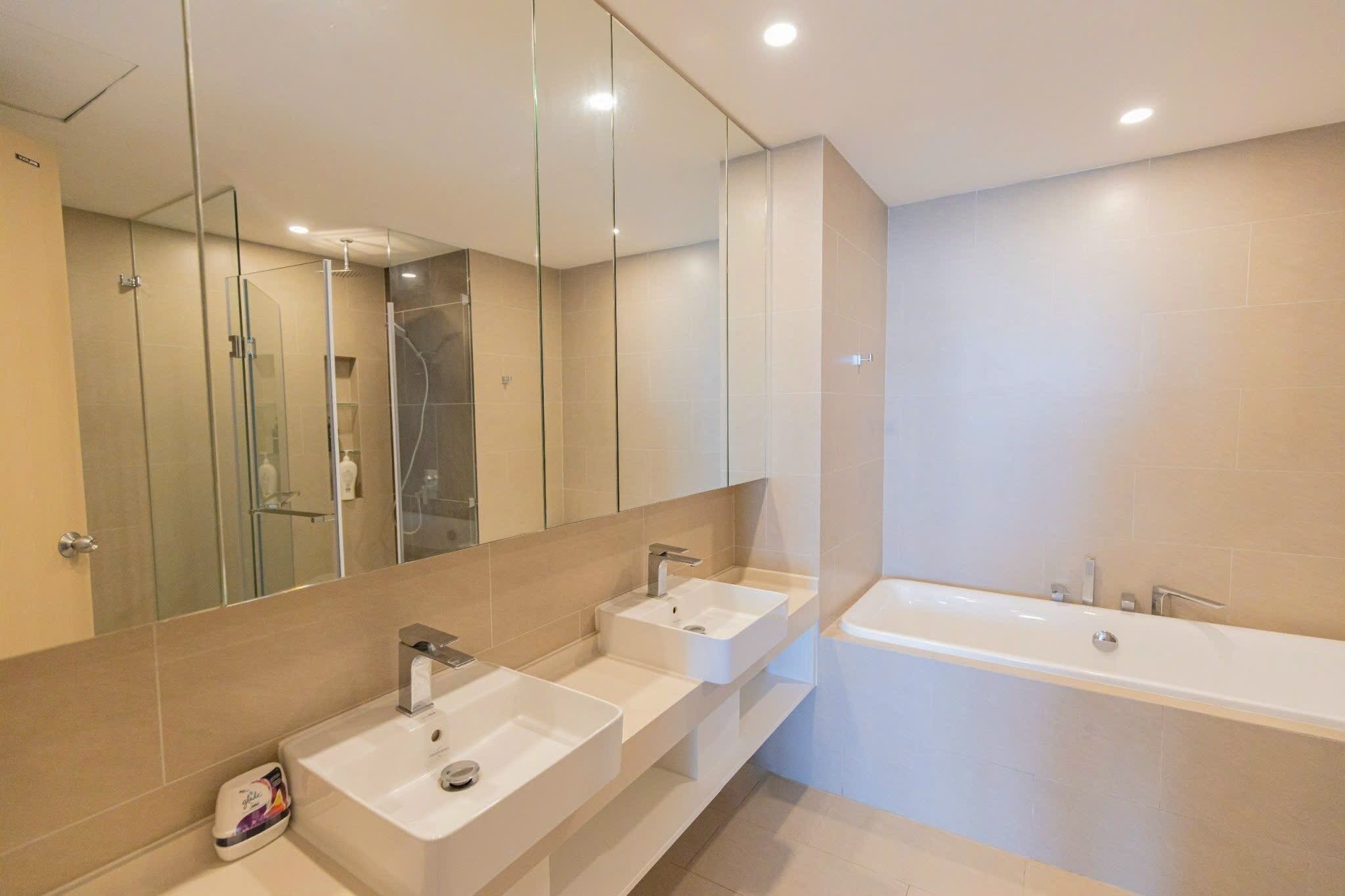 A modern bathroom with three sinks, a large mirror, and a bathtub.