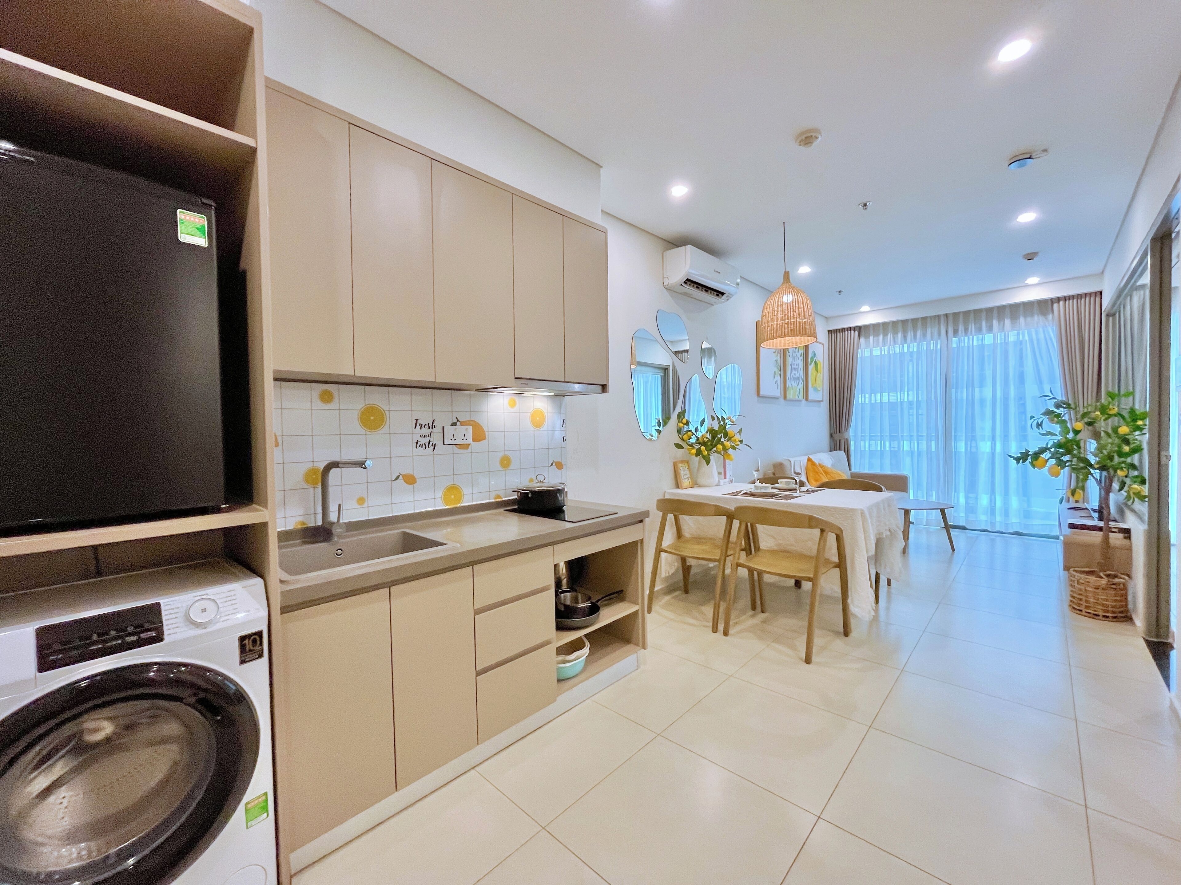 A modern kitchen with a washing machine, a dining area with a table and chairs, and a living area with a sofa and a large window.