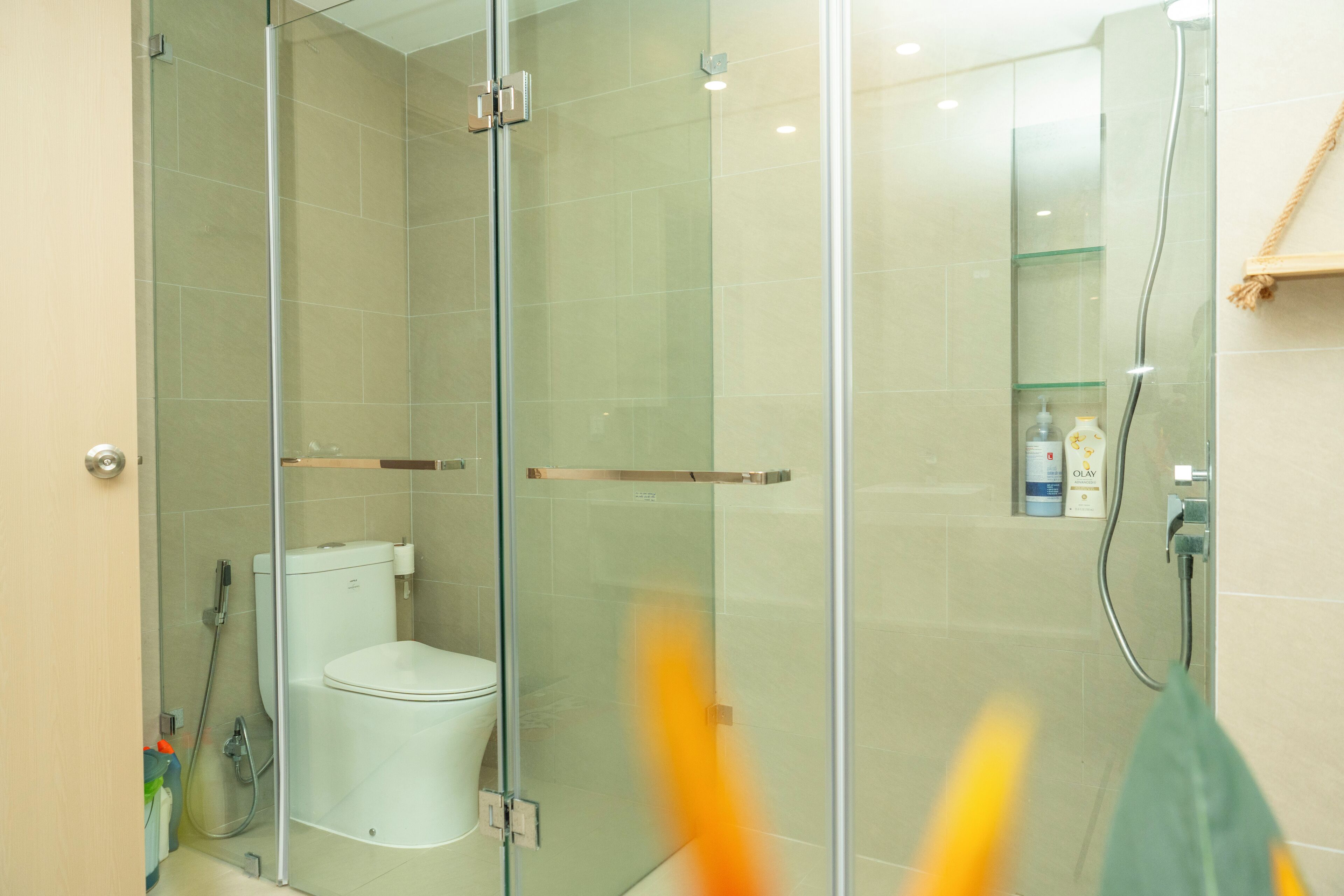 A modern bathroom with a glass-enclosed shower, a toilet, and a glass shelf with toiletries.