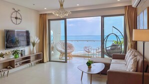 Amplia sala de estar con televisor grande, sofá, mesa de centro y balcón con vista al mar.