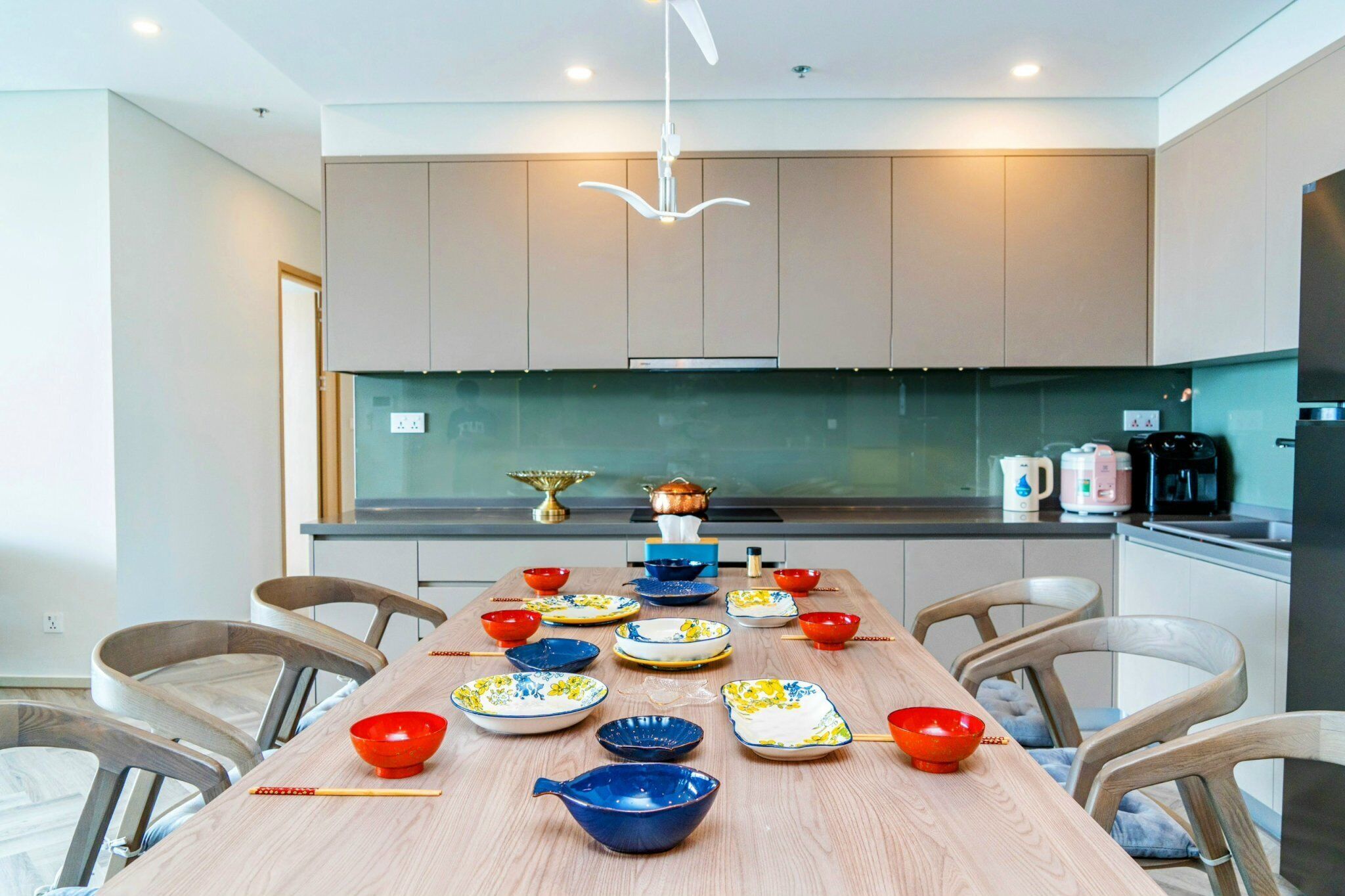 A modern kitchen with a dining table set for a meal, featuring various bowls and plates.