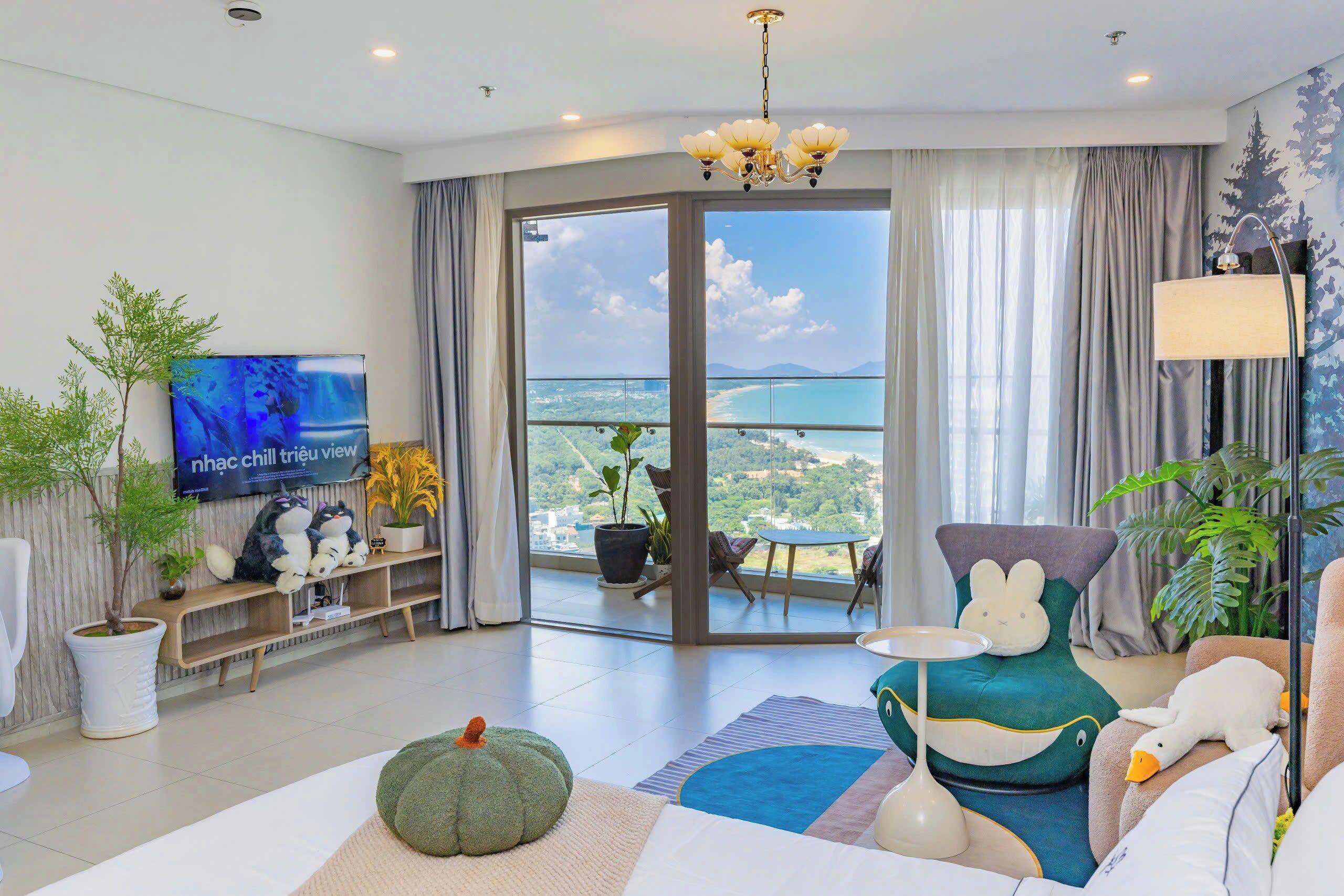Een moderne woonkamer met een grote televisie, comfortabele zitplaatsen, uitzicht op zee en een balkon met planten.