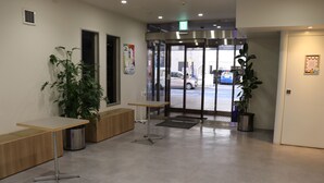A reception area with a wooden bench, a potted plant, and a glass door leading outside. - YOU STYLE HOTEL MATE (Kagoshima)