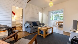 Sala de estar com sofá, mesa de centro e televisão. Uma janela oferece luz natural e vista para o exterior.