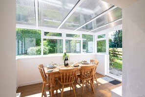 A conservatory with a table set for dining, surrounded by large windows. - Ty Capel Bach: A pet-friendly cottage in Hermon (Bodorgan)