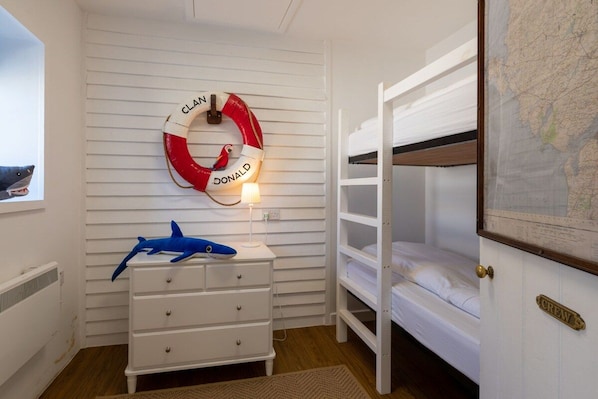 A room with bunk beds, a dresser, a life preserver, and a map on the wall.