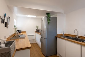 Cocina moderna con refrigerador de acero inoxidable, encimeras de madera, un lavamanos y una planta encima del refrigerador.