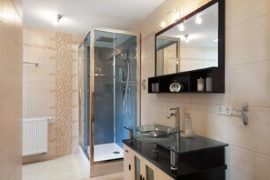 A modern bathroom with a glass-enclosed shower, a glass sink, and a mirror above the sink.