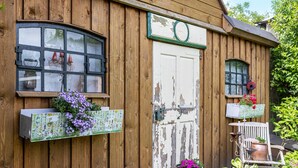 A wooden building with a white door, windows with black frames, and flower boxes with purple flowers. - Holiday Home 'Ferienhaus 75 Qm, 1 Schlafzimmer' with Private Terrace, Shared Garden and Wi-Fi (Neuruppin)