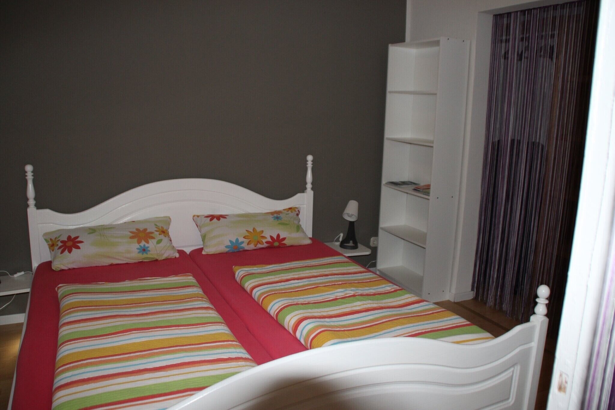 A bed with a white headboard, two pillows, a striped bedspread, and a red blanket.