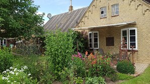 Une maison en briques avec un jardin, une antenne parabolique et une fenêtre ornée d’un cadre décoratif.