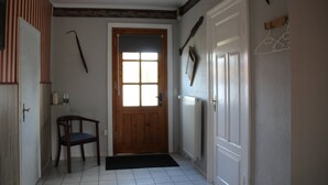 Un couloir avec une porte en bois, une chaise, un radiateur et un porte-manteau.