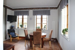 Un coin repas comprenant une table ronde, quatre chaises, un téléviseur et des fenêtres avec des rideaux.