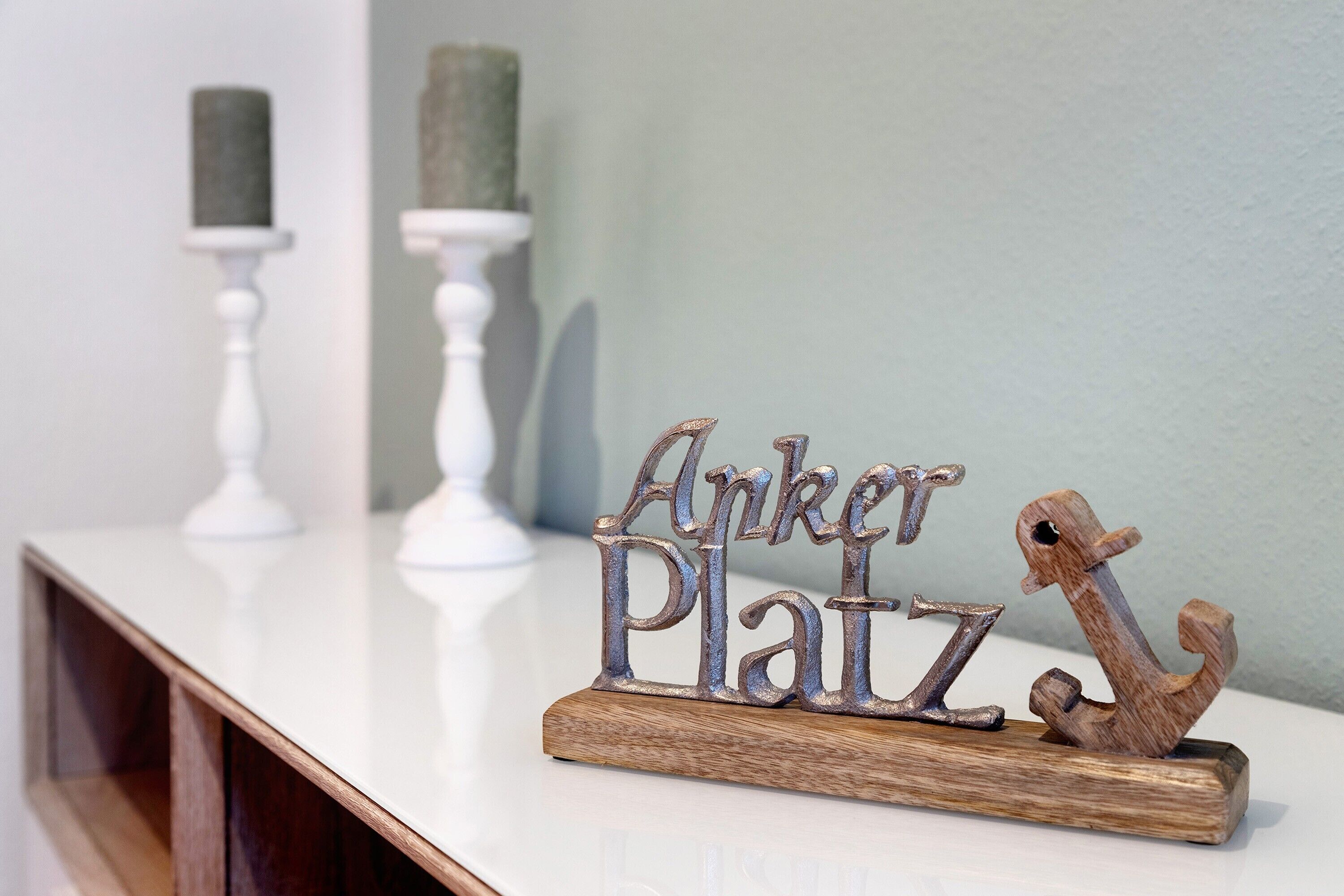 Una placa de madera con la inscripción 'Anker Platz' y un ancla de barco sobre una mesa blanca frente a una pared clara.