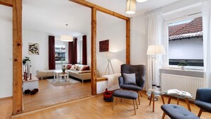 Een moderne woonkamer met een houten vloer, een bank, een fauteuil, een glazen tafel en een raam met uitzicht.