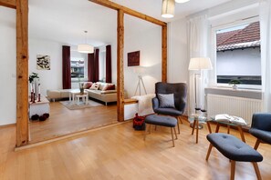 Ein modernes Wohnzimmer mit Holzboden, einer Couch, einem Sessel, einem Glastisch und einem Fenster mit Aussicht.