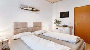 Een tweepersoonsbed met hoofdbord, nachtkastjes, een houten dressoir, een wanddecoratie en een houten deur.