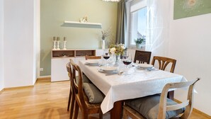 Een eetgedeelte met een tafel voor vier personen, houten stoelen, een witte tafelkleed en een vaas met bloemen.