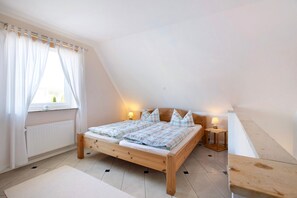 Une chambre à coucher avec un lit en bois, des rideaux blancs, une fenêtre, une table de chevet avec une lampe et un radiateur.