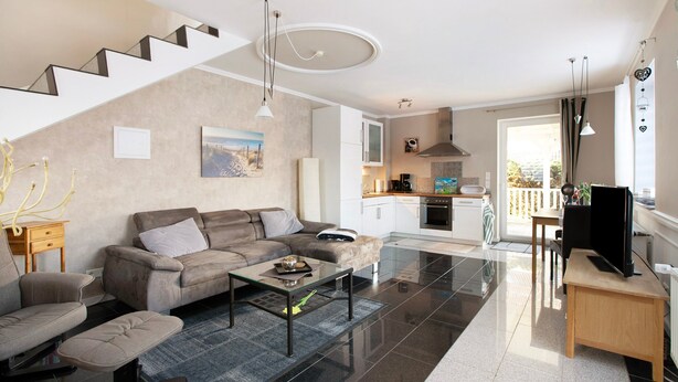 A modern living room with a sofa, coffee table, and TV stand. A staircase leads to a kitchen area with a dining table and chairs. - Apartment 'Wendtlandt' with Private Terrace and Wi-Fi (Kappeln)