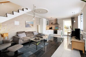 Ein modernes Wohnzimmer mit Sofa, Couchtisch und TV-Möbel. Eine Treppe führt zu einem Küchenbereich mit Esstisch und Stühlen.
