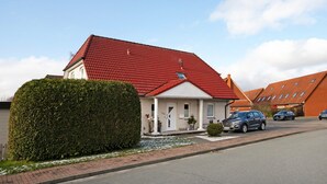 A residential house with a red roof, a well-maintained hedge, and a driveway with parked cars. - Apartment 'Wendtlandt' with Private Terrace and Wi-Fi (Kappeln)