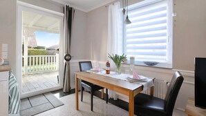 A dining area with a table, chairs, a window with blinds, a door leading outside, and a television on a stand. - Apartment 'Wendtlandt' with Private Terrace and Wi-Fi (Kappeln)