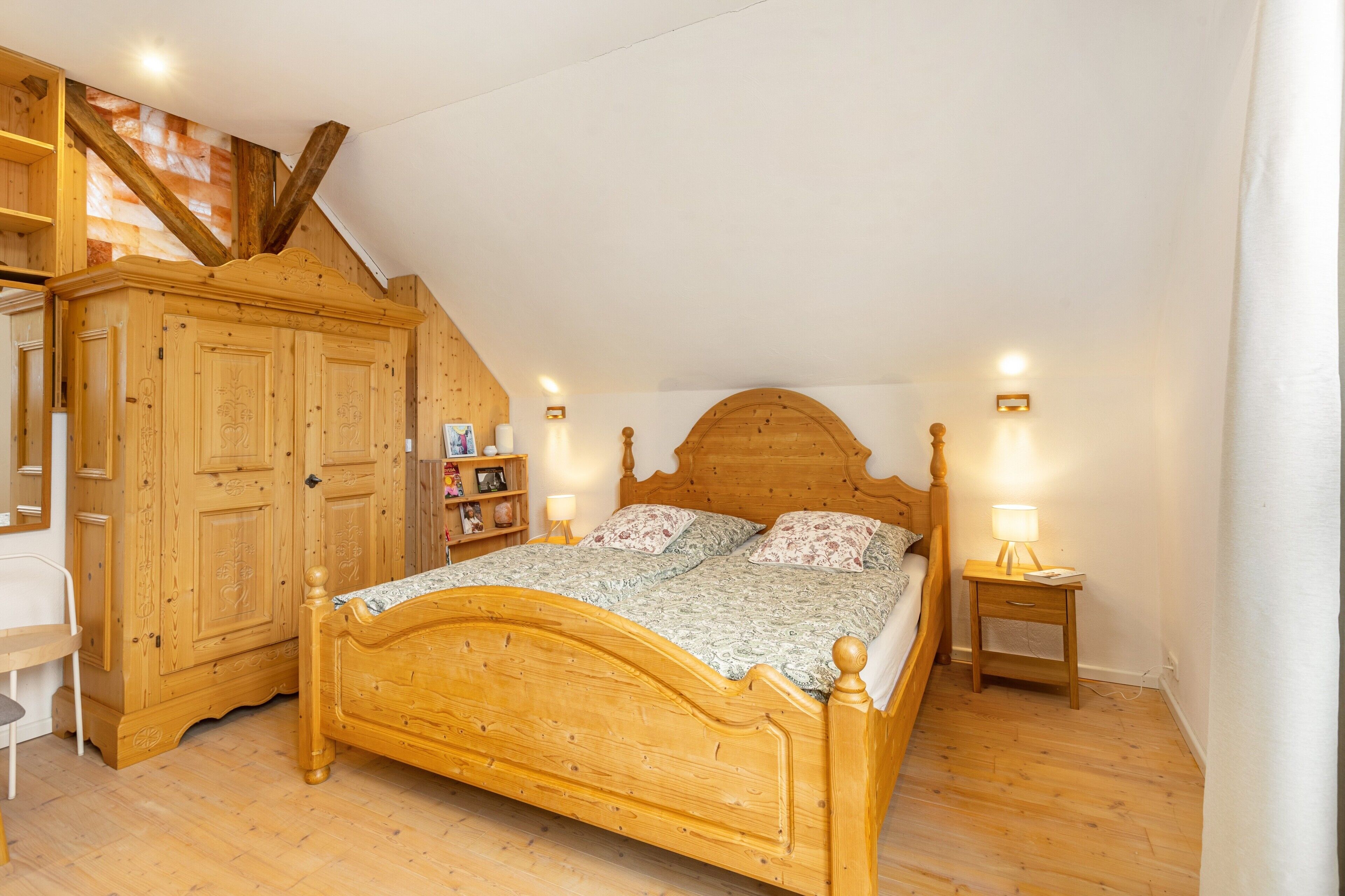 Ein Schlafzimmer mit einem hölzernen Bett, einem Kleiderschrank, einem Schreibtisch und einem Nachttisch mit Lampe.