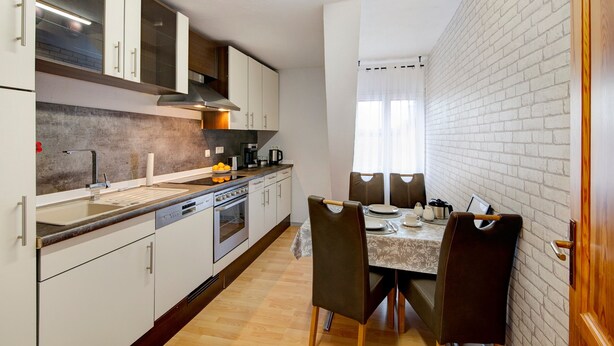 Cocina compacta con electrodomésticos modernos, comedor con mesa y sillas, y pared de ladrillo.