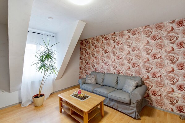 Sala de estar com sofá, mesa de centro, planta em vaso e parede com padrão floral de rosas.