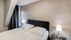 Habitación de hotel con cama, dos mesitas de noche, lámpara y ventana con cortina.