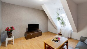 Una habitación con una televisión de pantalla plana, una mesa de comedor de madera, un sofá, una planta en maceta y una pequeña mesa blanca.