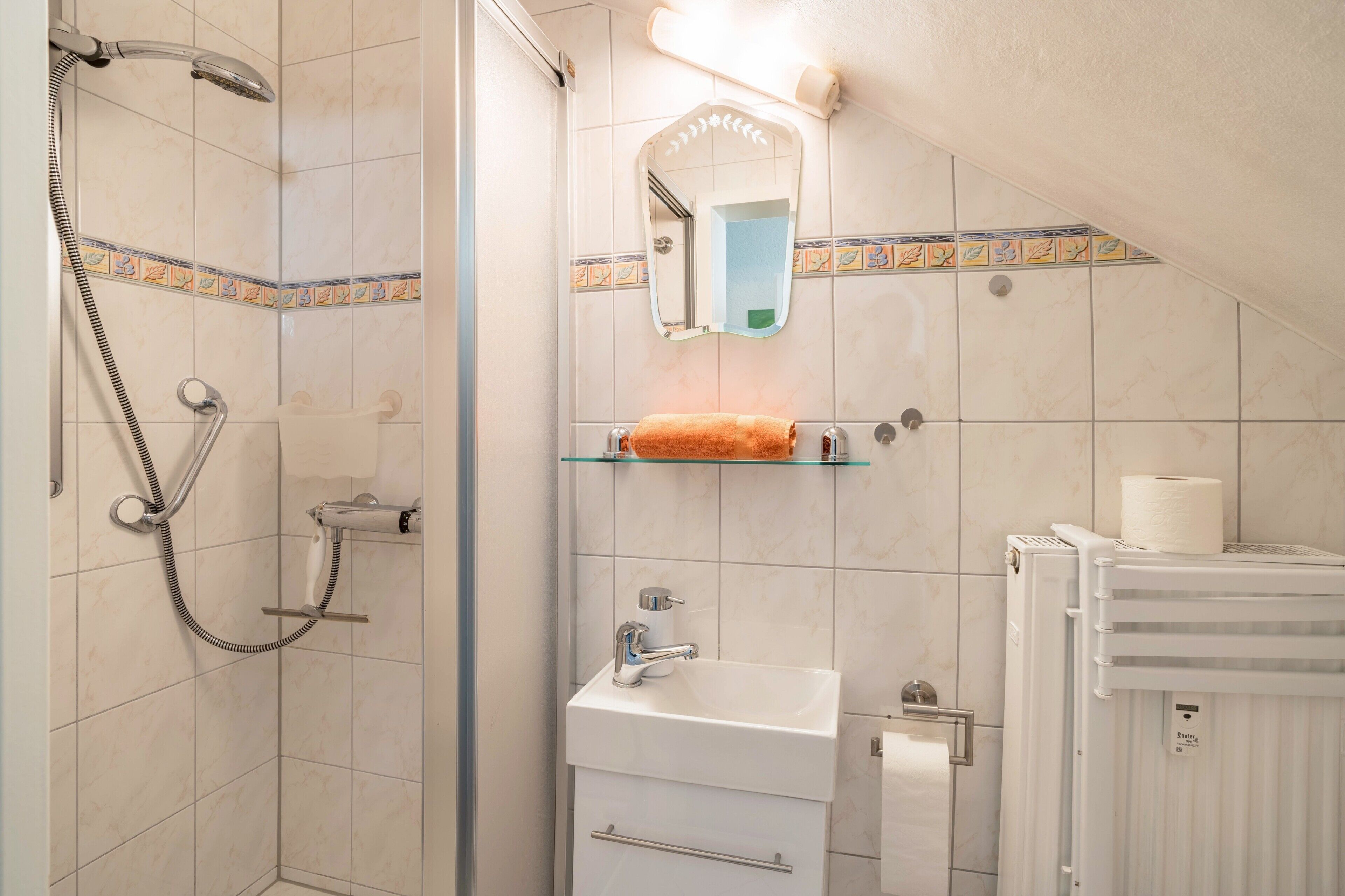 A bathroom with a shower, sink, mirror, and towel rack.