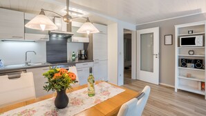 A modern kitchen with white cabinets, a dining table with a floral tablecloth, a vase with flowers, and a wine bottle. - Holiday Apartment Odenwald with Terrace and Wi-Fi (Wald-Michelbach)