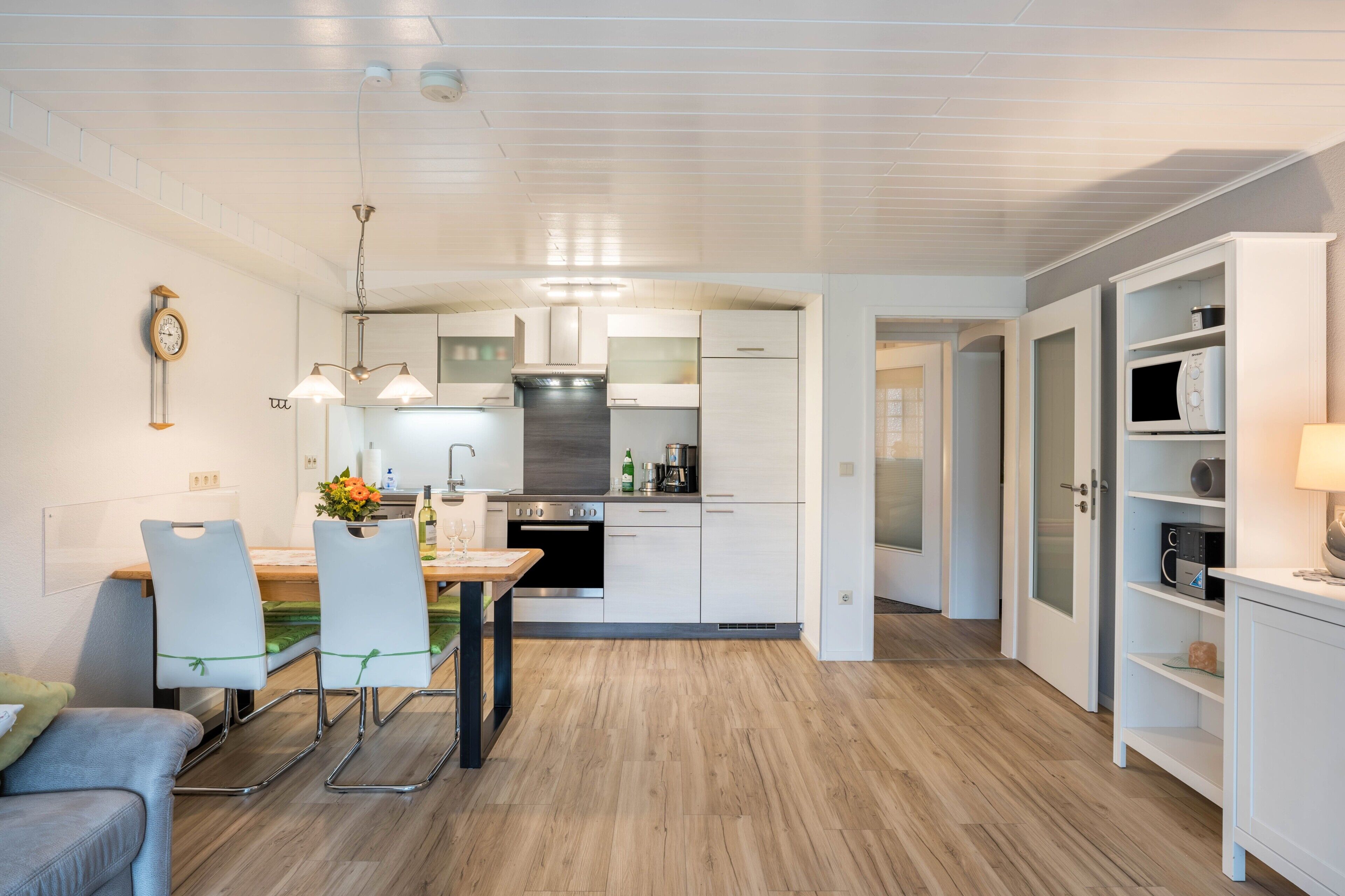 Una cocina moderna con armarios blancos, un comedor con mesa y sillas, y una sala de estar con sofá.