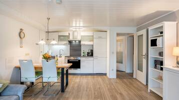 Una cocina moderna con armarios blancos, un comedor con mesa y sillas, y una sala de estar con sofá.