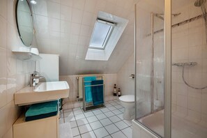 Een badkamer met dakraam, douche, toilet en wastafel.