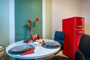 Een eettafel met borden, glazen, een broodrooster en een vaas met bloemen. Een rode koelkast staat rechts.
