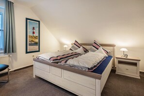 Een slaapkamer met een bed, nachtkastjes, een lamp, een ingelijst beeld aan de muur en een raam met gordijnen.