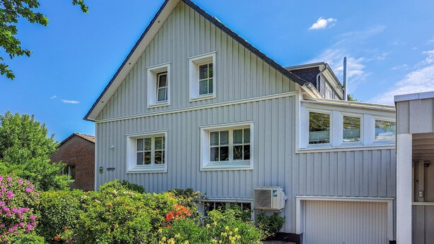 Ein zweistöckiges Haus mit Garage, umgeben von einem Garten mit verschiedenen Pflanzen und Blumen.
