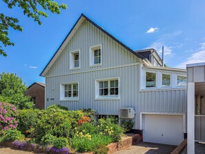 Een tweelaags huis met een garage, omgeven door een tuin vol planten en bloemen.